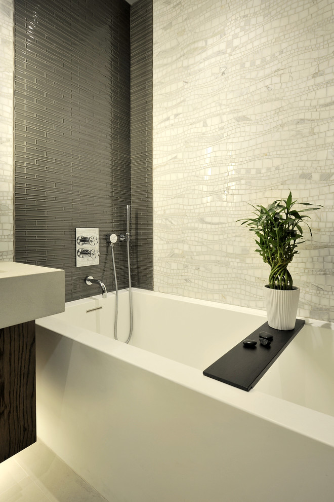 Ejemplo de cuarto de baño principal moderno con lavabo integrado, armarios con paneles lisos, puertas de armario de madera en tonos medios, bañera empotrada, ducha empotrada, paredes grises, baldosas y/o azulejos grises y baldosas y/o azulejos blancos