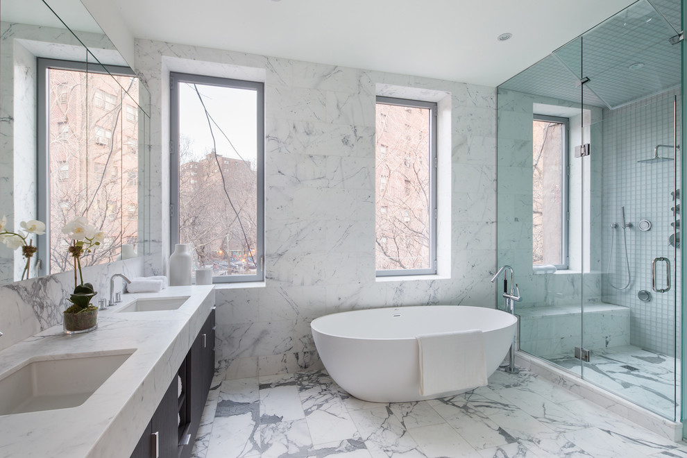 Contemporary bathroom in New York with a submerged sink, flat-panel cabinets, a freestanding bath, an alcove shower, grey tiles and white walls.