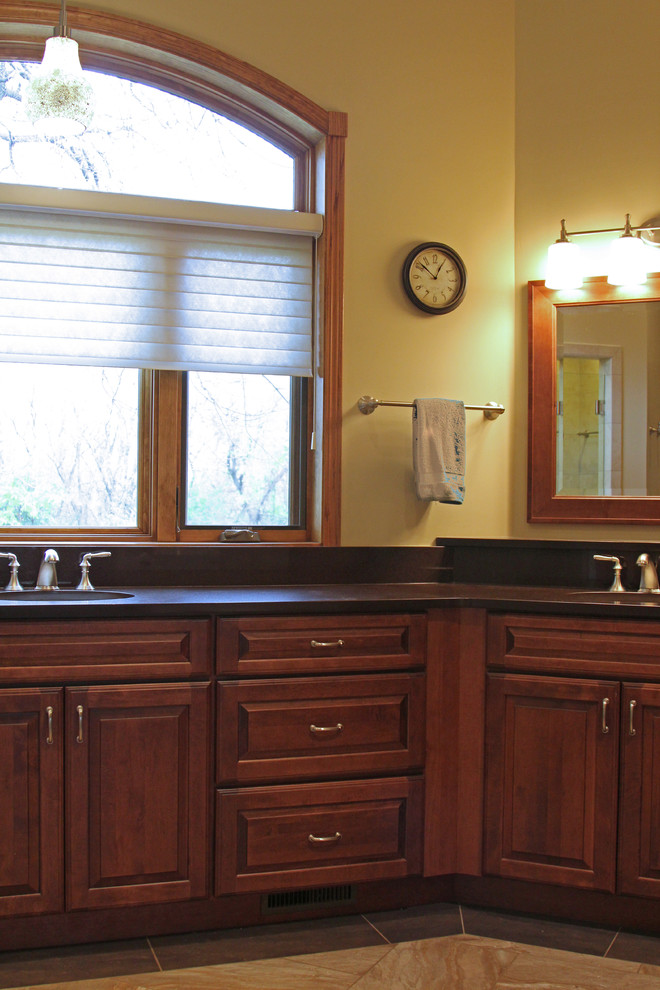 Photo of a large traditional ensuite bathroom in Milwaukee with raised-panel cabinets, dark wood cabinets, quartz worktops, brown worktops, an alcove shower, a one-piece toilet, beige walls, ceramic flooring, a submerged sink, beige floors and a hinged door.