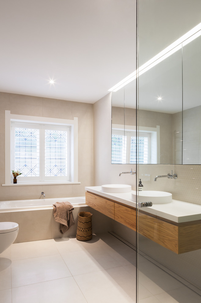 Design ideas for a medium sized contemporary family bathroom in Sydney with medium wood cabinets, beige tiles, beige walls, beige floors, a wall mounted toilet, mosaic tiles, a pedestal sink, wooden worktops and flat-panel cabinets.