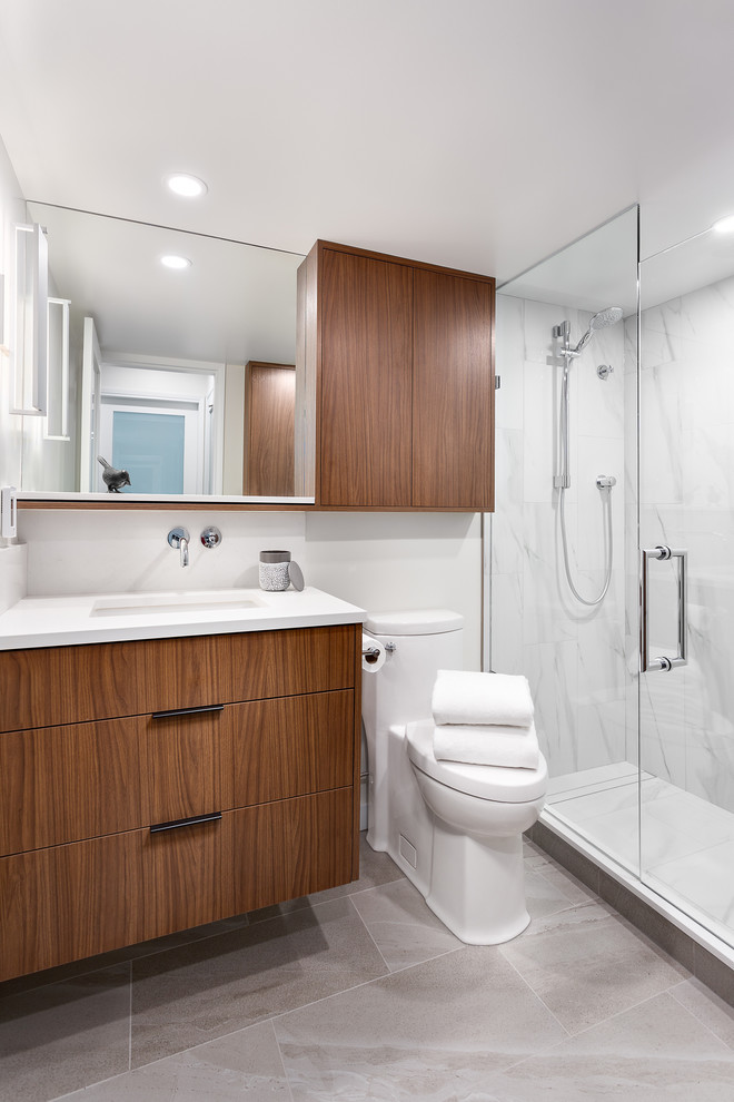Idéer för att renovera ett mellanstort funkis vit vitt badrum med dusch, med släta luckor, skåp i mellenmörkt trä, vit kakel, dusch med gångjärnsdörr, en dusch i en alkov, en toalettstol med hel cisternkåpa, marmorkakel, vita väggar, klinkergolv i porslin, ett undermonterad handfat, bänkskiva i kvartsit och grått golv