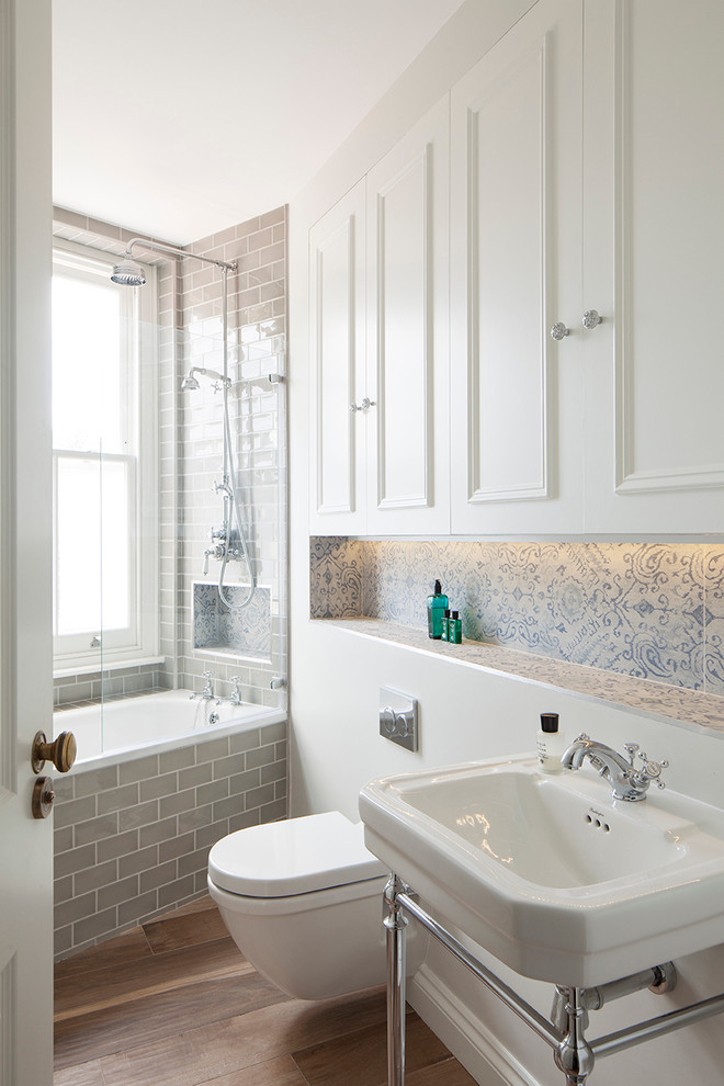Ornate porcelain tile medium tone wood floor bathroom photo in London with a console sink, white cabinets, a wall-mount toilet and recessed-panel cabinets