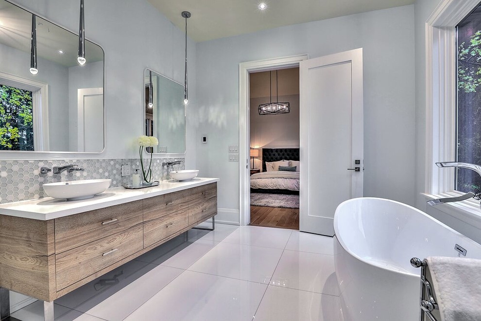 Large trendy master gray tile and ceramic tile ceramic tile and white floor freestanding bathtub photo in Toronto with flat-panel cabinets, medium tone wood cabinets, a two-piece toilet, white walls, a vessel sink, solid surface countertops and white countertops