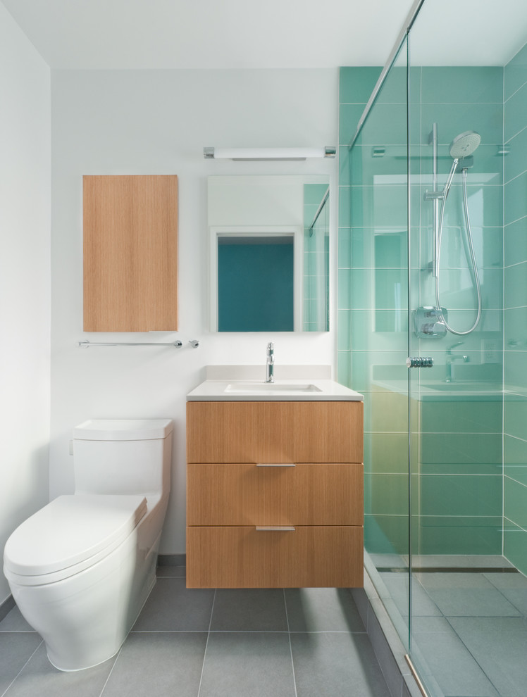 Cette image montre une douche en alcôve design en bois clair avec un lavabo encastré, un placard à porte plane, WC à poser, un carrelage bleu et un carrelage en pâte de verre.