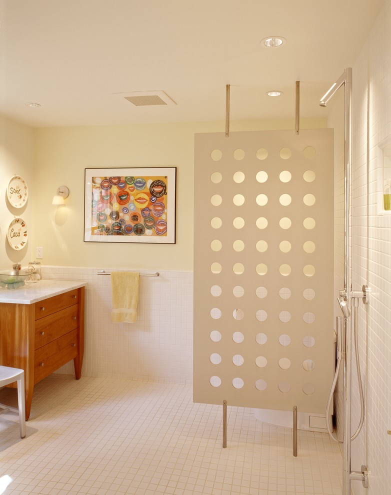 Inredning av ett modernt badrum, med en kantlös dusch, skåp i mellenmörkt trä, bänkskiva i akrylsten, vit kakel, keramikplattor, ett fristående handfat och släta luckor
