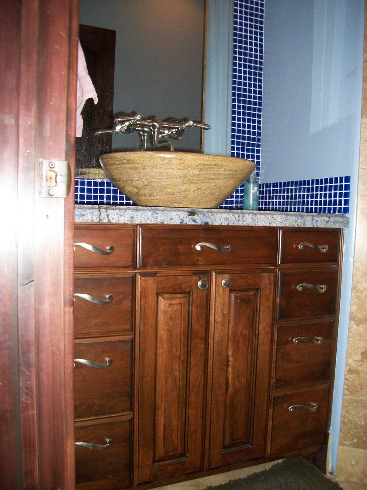 Foto de cuarto de baño clásico de tamaño medio con lavabo sobreencimera, armarios tipo mueble, puertas de armario de madera oscura, encimera de granito, baldosas y/o azulejos azules, baldosas y/o azulejos de vidrio, paredes azules y aseo y ducha