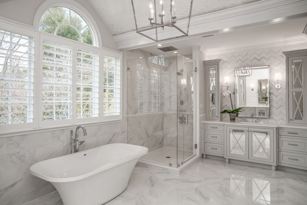 Идея дизайна: большая главная ванная комната в стиле неоклассика (современная классика) с стеклянными фасадами, серыми фасадами, отдельно стоящей ванной, угловым душем, белой плиткой, мраморной плиткой, мраморной столешницей, белыми стенами, мраморным полом и врезной раковиной