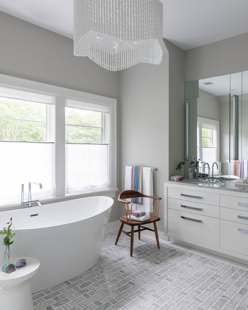 Photo of a coastal bathroom in New York with flat-panel cabinets, white cabinets, a freestanding bath, grey walls, a submerged sink, grey floors, grey worktops and a built in vanity unit.