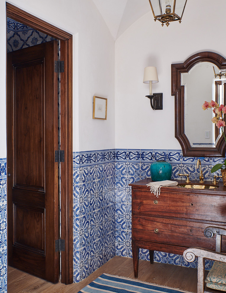 Mediterranes Badezimmer mit hellbraunen Holzschränken, blauen Fliesen, weißen Fliesen, weißer Wandfarbe, braunem Holzboden, Unterbauwaschbecken, Waschtisch aus Holz, braunem Boden, brauner Waschtischplatte und flächenbündigen Schrankfronten in Santa Barbara