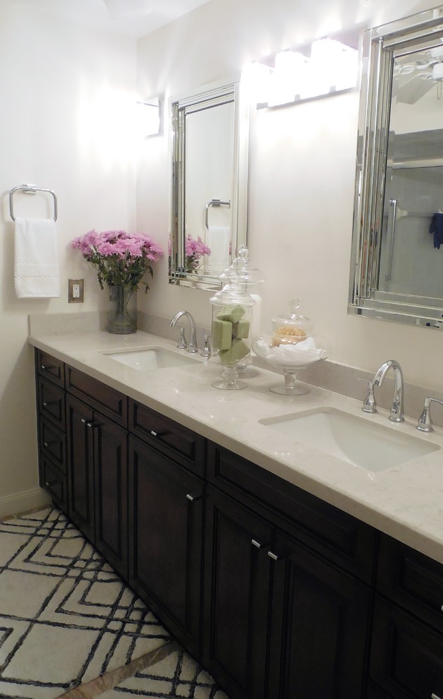 Cette image montre une salle de bain principale design en bois foncé de taille moyenne avec un placard avec porte à panneau surélevé, un mur blanc, un lavabo encastré et un plan de toilette en marbre.