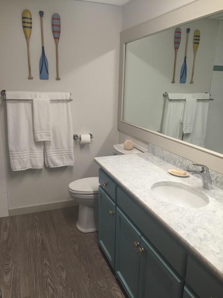 Maritim inredning av ett litet badrum med dusch, med skåp i shakerstil, blå skåp, en dusch i en alkov, en toalettstol med separat cisternkåpa, vita väggar, mörkt trägolv, ett undermonterad handfat, laminatbänkskiva, brunt golv och dusch med duschdraperi