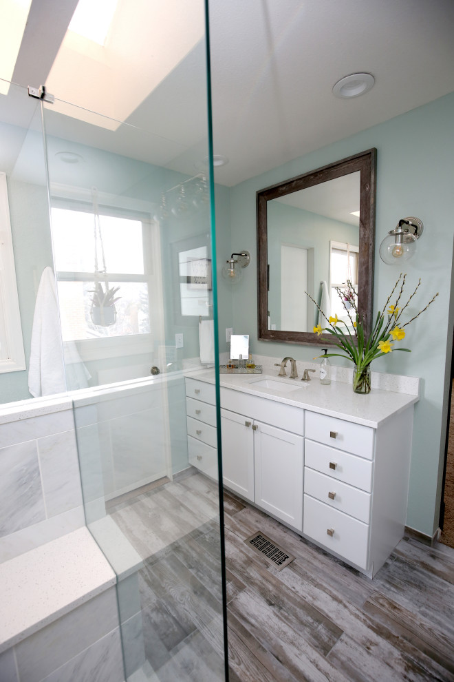 Cette image montre une petite salle de bain principale marine avec un placard avec porte à panneau surélevé, des portes de placard blanches, une douche d'angle, un carrelage bleu, des carreaux de céramique, un mur vert, un sol en carrelage de porcelaine, un lavabo encastré, un sol marron, une cabine de douche à porte battante, un plan de toilette blanc, meuble double vasque et meuble-lavabo encastré.