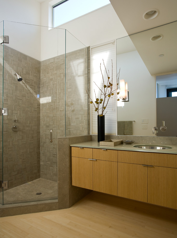 Cette image montre une salle de bain minimaliste en bois brun de taille moyenne avec un lavabo encastré, un placard à porte plane, une douche d'angle, un carrelage de pierre, un mur blanc, parquet en bambou, un plan de toilette en verre et un carrelage gris.