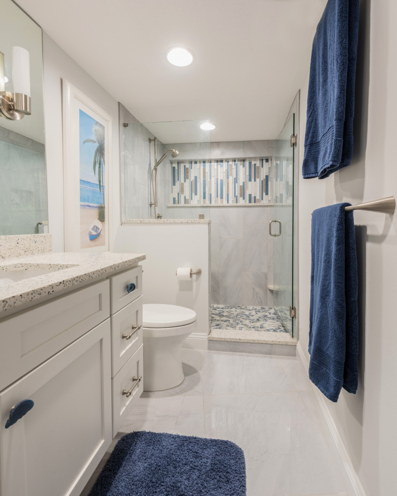 Пример оригинального дизайна: главная ванная комната среднего размера в морском стиле с фасадами с утопленной филенкой, белыми фасадами, душем в нише, серой плиткой, керамогранитной плиткой, серыми стенами, полом из керамогранита, врезной раковиной, столешницей из переработанного стекла, серым полом, душем с распашными дверями и белой столешницей