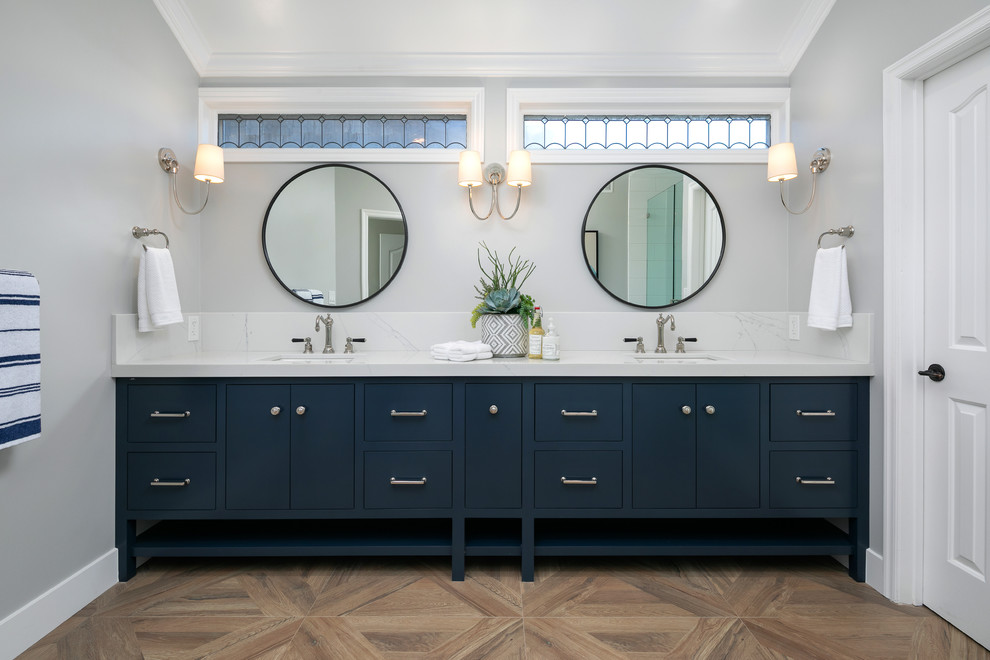 Foto de cuarto de baño principal costero con puertas de armario azules, paredes grises, lavabo bajoencimera, suelo marrón, encimeras blancas y armarios con paneles lisos
