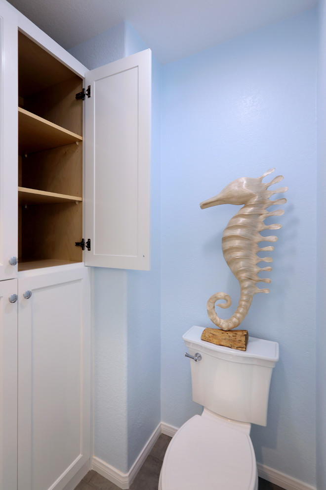 Exemple d'une salle de bain principale bord de mer de taille moyenne avec un placard à porte shaker, des portes de placard blanches, une baignoire en alcôve, un combiné douche/baignoire, WC séparés, un carrelage bleu, des carreaux de porcelaine, un mur bleu, un sol en carrelage de porcelaine, un plan de toilette en marbre, un sol gris et un lavabo encastré.