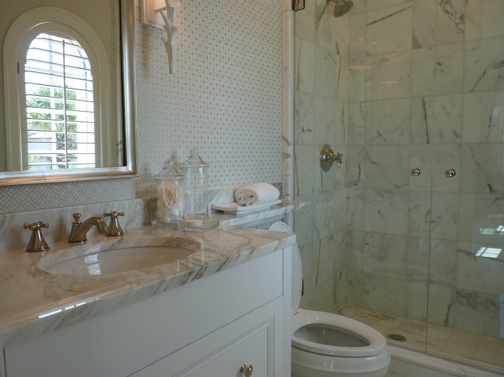 Inredning av ett maritimt stort badrum, med ett integrerad handfat, luckor med infälld panel, vita skåp, marmorbänkskiva, en dusch/badkar-kombination och en toalettstol med hel cisternkåpa