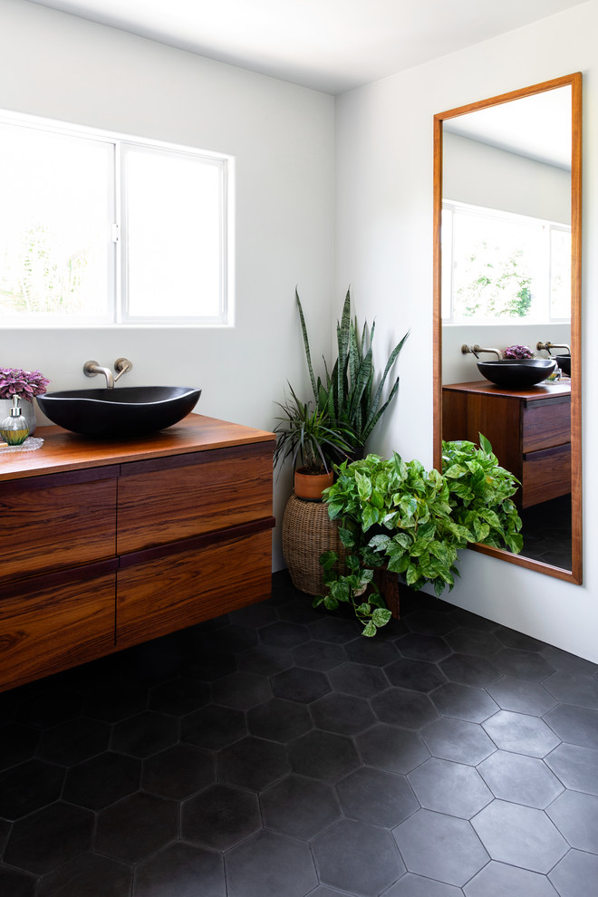This is an example of a large modern ensuite bathroom in San Diego with flat-panel cabinets, medium wood cabinets, white walls, cement flooring, a vessel sink, wooden worktops and black floors.