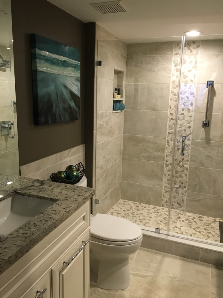 Inspiration for a large tropical 3/4 gray tile and porcelain tile pebble tile floor and beige floor alcove shower remodel in Other with raised-panel cabinets, white cabinets, a two-piece toilet, gray walls, an undermount sink, a hinged shower door, granite countertops and gray countertops