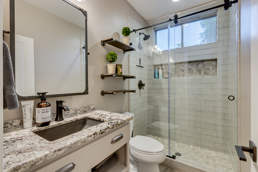 Idéer för att renovera ett litet industriellt badrum med dusch, med släta luckor, grå skåp, en öppen dusch, en toalettstol med separat cisternkåpa, grå kakel, keramikplattor, grå väggar, klinkergolv i keramik, ett undermonterad handfat, granitbänkskiva, grått golv och dusch med skjutdörr
