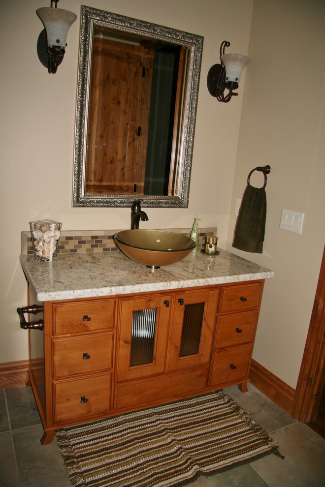Aménagement d'une salle de bain montagne en bois brun avec une vasque, un placard avec porte à panneau surélevé, un plan de toilette en granite, un carrelage beige, des carreaux de porcelaine et un sol en carrelage de porcelaine.