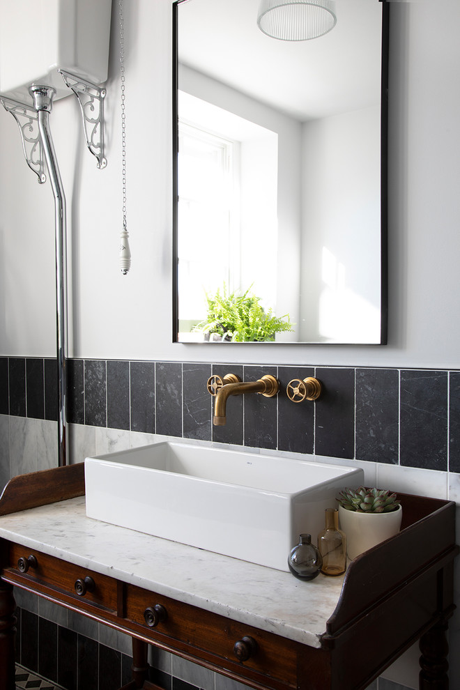 Klassisches Badezimmer mit hellbraunen Holzschränken, Wandtoilette mit Spülkasten, schwarzen Fliesen, weißen Fliesen, weißer Wandfarbe, Aufsatzwaschbecken und weißer Waschtischplatte in London