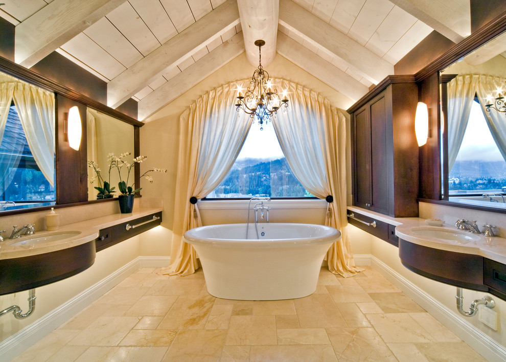 This is an example of an expansive mediterranean ensuite bathroom in Other with a freestanding bath, beige tiles, dark wood cabinets, brown walls, travertine flooring, brown floors and a submerged sink.