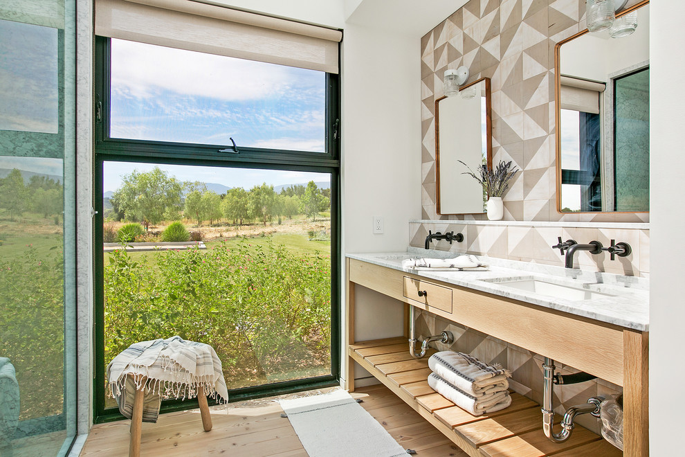 Country bathroom in Los Angeles with open cabinets, medium wood cabinets, beige tiles, brown tiles, white tiles, white walls, medium hardwood flooring, a submerged sink, brown floors and white worktops.