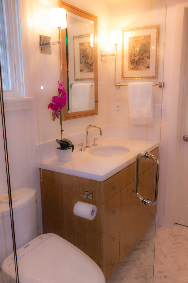 Immagine di una piccola stanza da bagno con doccia minimalista con ante lisce, ante in legno chiaro, doccia alcova, WC monopezzo, pavimento in marmo, lavabo sottopiano, top in quarzite, pavimento grigio, porta doccia a battente e top bianco
