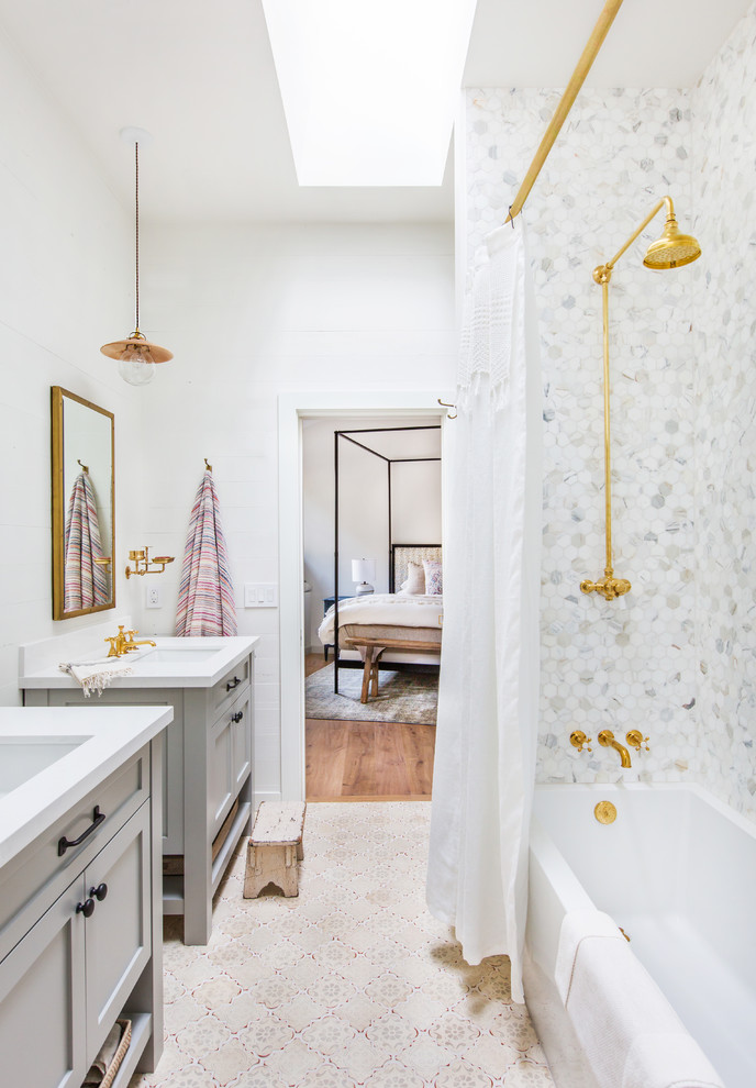 Photo of a coastal bathroom in Los Angeles with recessed-panel cabinets, grey cabinets, an alcove bath, a shower/bath combination, grey tiles, white tiles, mosaic tiles, white walls, a submerged sink, beige floors and a shower curtain.