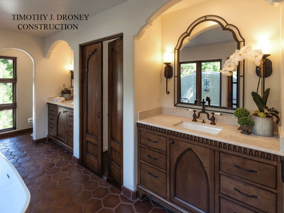 Photo of a small mediterranean ensuite bathroom in Los Angeles with freestanding cabinets, distressed cabinets, a freestanding bath, a corner shower, white tiles, ceramic tiles, white walls, terracotta flooring, a submerged sink, limestone worktops, brown floors, a hinged door and beige worktops.