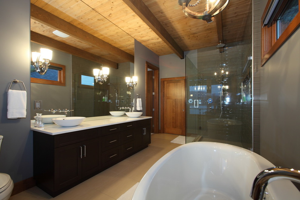 Design ideas for a large classic ensuite bathroom in Vancouver with a vessel sink, shaker cabinets, dark wood cabinets, engineered stone worktops, a freestanding bath, a double shower, a one-piece toilet, grey tiles, ceramic tiles, grey walls and ceramic flooring.