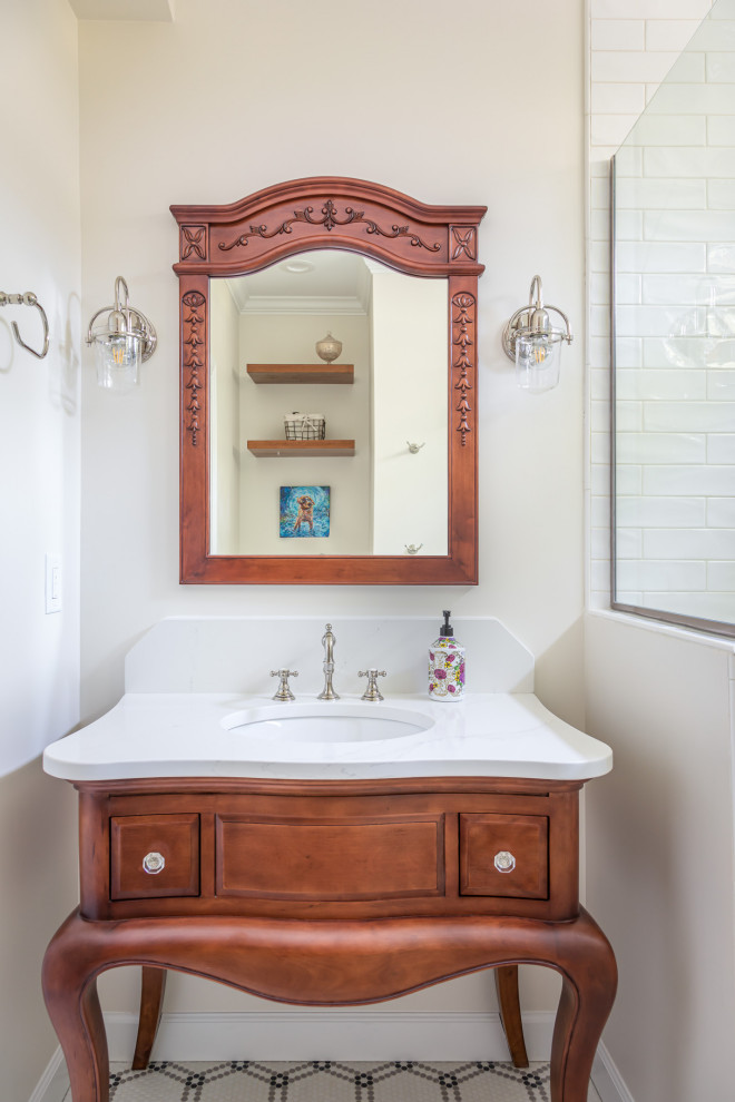 Klassisches Badezimmer mit hellbraunen Holzschränken, weißen Fliesen, beiger Wandfarbe, Mosaik-Bodenfliesen, Unterbauwaschbecken, buntem Boden, weißer Waschtischplatte und profilierten Schrankfronten in Raleigh