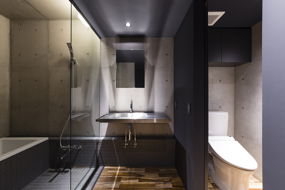 Cette photo montre une salle de bain tendance avec une baignoire d'angle, une douche ouverte, un carrelage gris, un mur gris, parquet foncé, un plan vasque, un plan de toilette en acier inoxydable, un sol marron et aucune cabine.