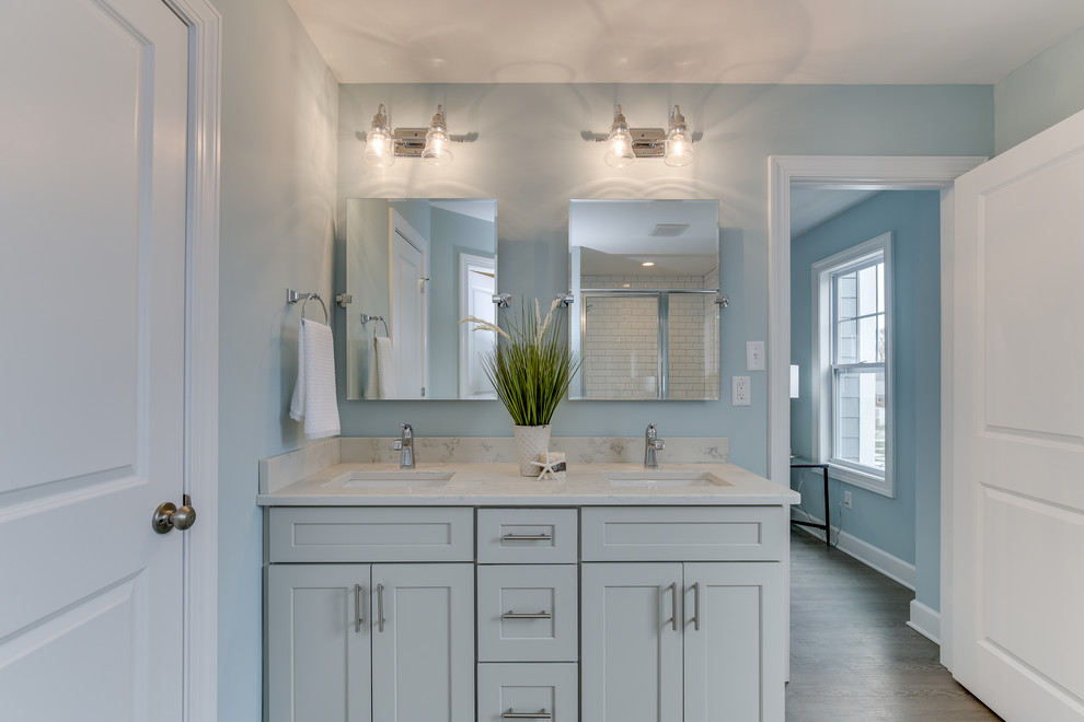 Inspiration for a mid-sized coastal master light wood floor and gray floor corner shower remodel in Other with shaker cabinets, gray cabinets, a one-piece toilet, blue walls, an undermount sink, quartz countertops, a hinged shower door and white countertops