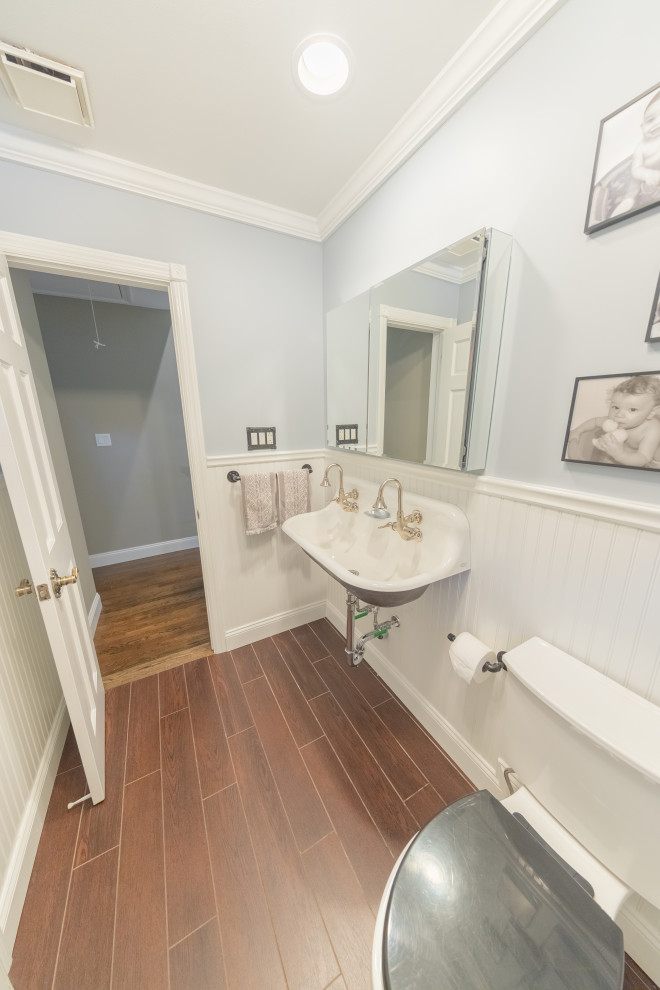 Design ideas for a medium sized traditional family bathroom in New York with an alcove bath, a shower/bath combination, a two-piece toilet, white tiles, grey walls, porcelain flooring, a wall-mounted sink, brown floors, a shower curtain, double sinks and wainscoting.