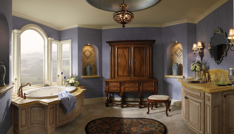 Стильный дизайн: большая главная ванная комната в викторианском стиле с фасадами с выступающей филенкой, искусственно-состаренными фасадами, угловой ванной, фиолетовыми стенами, полом из травертина, накладной раковиной и мраморной столешницей - последний тренд