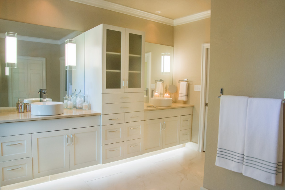 Cette photo montre une salle de bain principale tendance de taille moyenne avec un placard avec porte à panneau encastré, des portes de placard beiges, une baignoire indépendante, une douche d'angle, un carrelage beige, une plaque de galets, un mur beige, un sol en galet et une vasque.