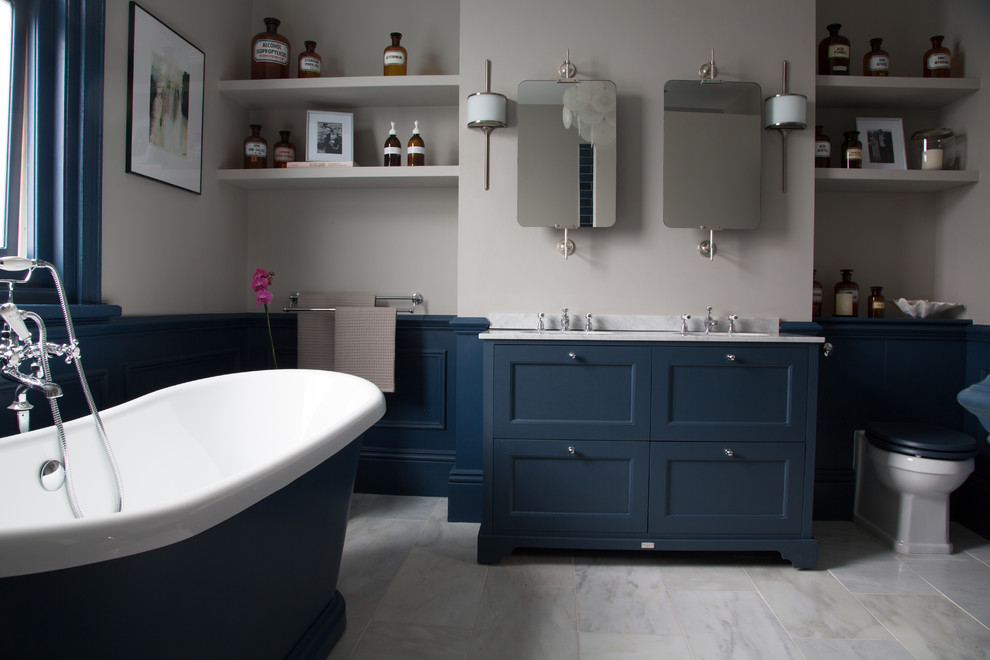 Ejemplo de cuarto de baño principal tradicional de tamaño medio con puertas de armario azules, bañera exenta, suelo de mármol, encimera de mármol, suelo gris, encimeras grises, lavabo bajoencimera y armarios con paneles empotrados