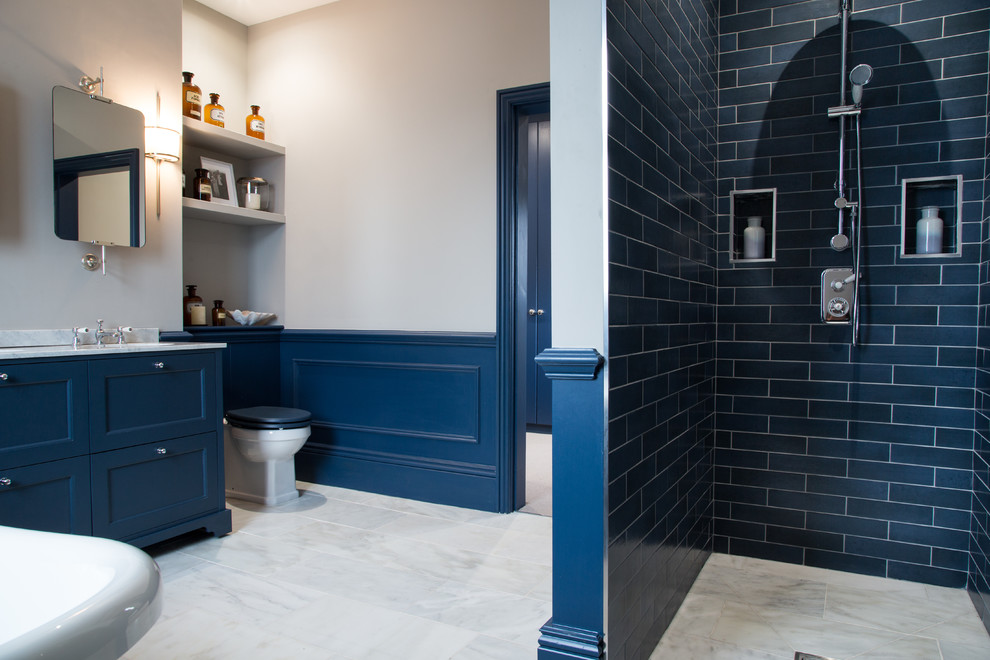 Photo of a medium sized traditional ensuite bathroom in Essex with freestanding cabinets, blue cabinets, a freestanding bath, an alcove shower, a one-piece toilet, marble flooring, a built-in sink, marble worktops, grey floors, an open shower and grey worktops.