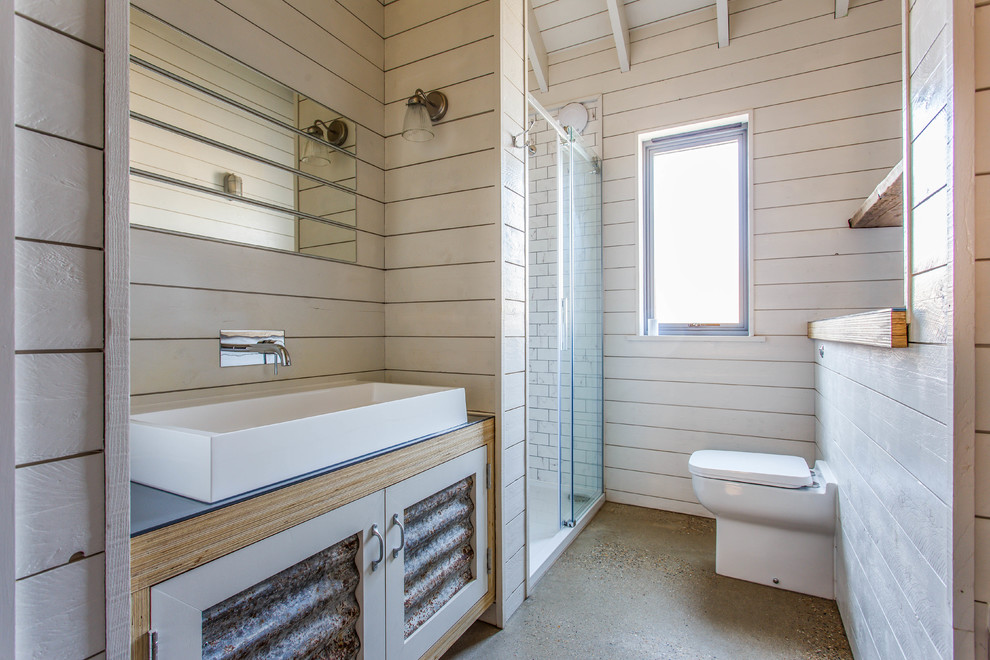 Diseño de cuarto de baño de estilo de casa de campo con ducha empotrada, sanitario de pared, paredes beige, suelo de cemento, lavabo sobreencimera, suelo gris, ducha con puerta corredera y encimeras grises