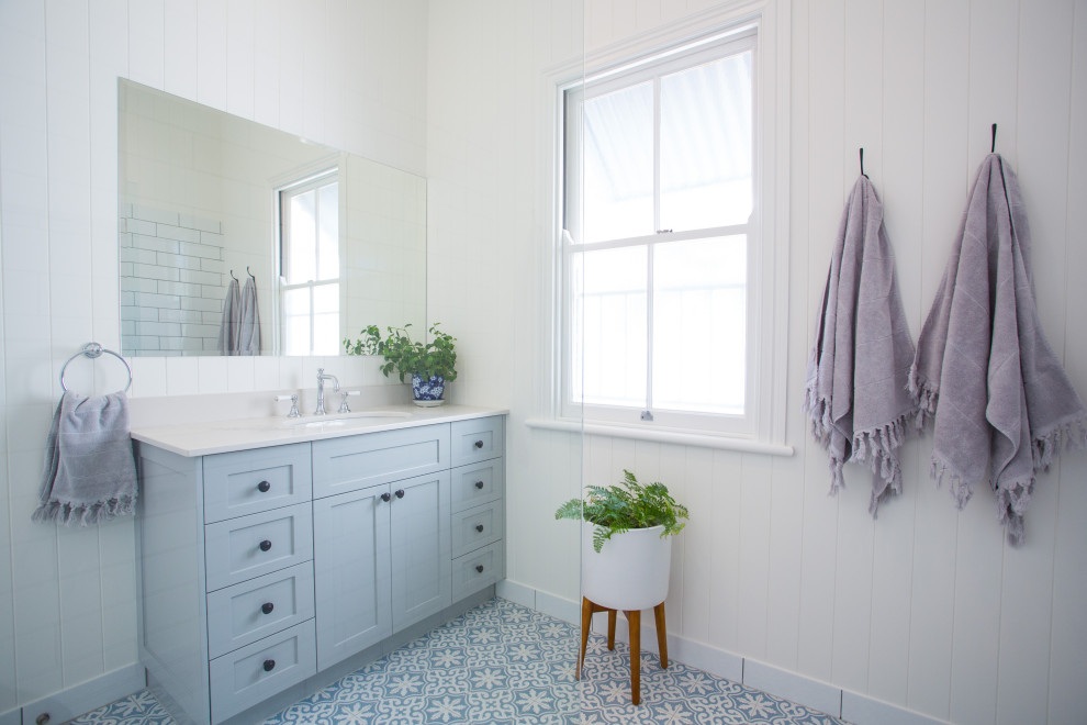 ブリスベンにある高級な広いコンテンポラリースタイルのおしゃれなマスターバスルーム (家具調キャビネット、グレーのキャビネット、置き型浴槽、コーナー設置型シャワー、一体型トイレ	、白いタイル、白い壁、セラミックタイルの床、オーバーカウンターシンク、大理石の洗面台、青い床、白い洗面カウンター) の写真