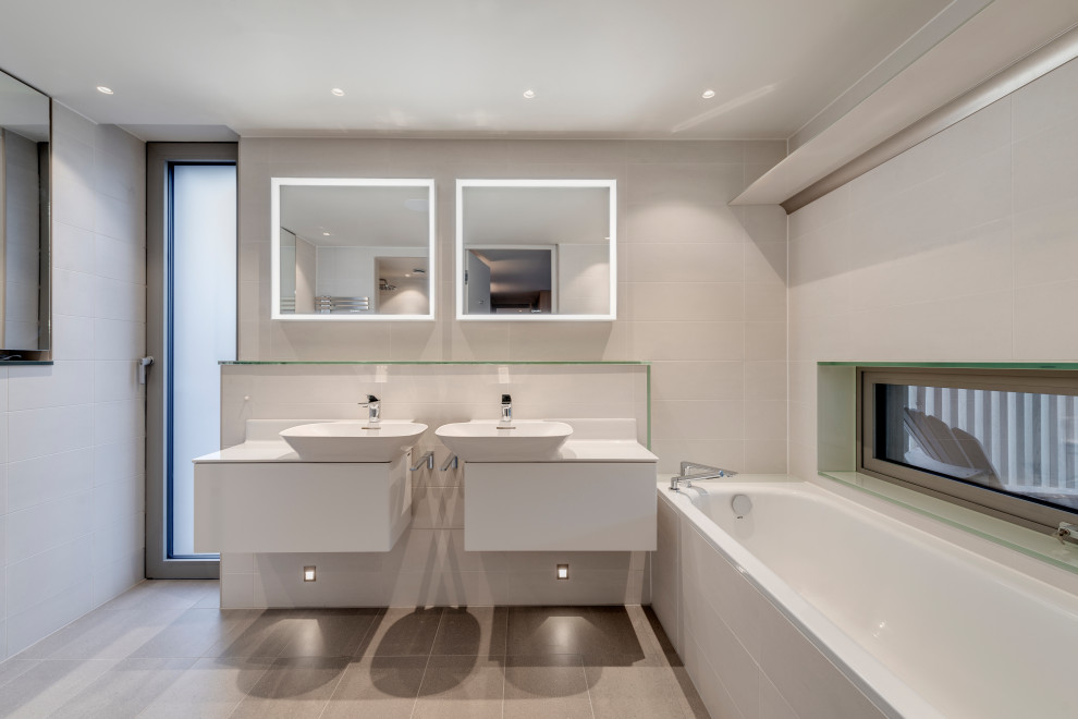 Immagine di una stanza da bagno minimal con ante lisce, ante bianche, vasca ad alcova, piastrelle grigie, lavabo a bacinella, pavimento grigio, top bianco, due lavabi e mobile bagno sospeso