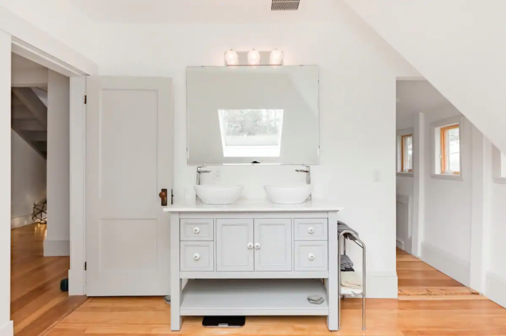 Freestanding bathtub - small 1950s master medium tone wood floor, double-sink and vaulted ceiling freestanding bathtub idea in Portland Maine with recessed-panel cabinets, gray cabinets, a two-piece toilet, white walls, a vessel sink, marble countertops, white countertops and a freestanding vanity