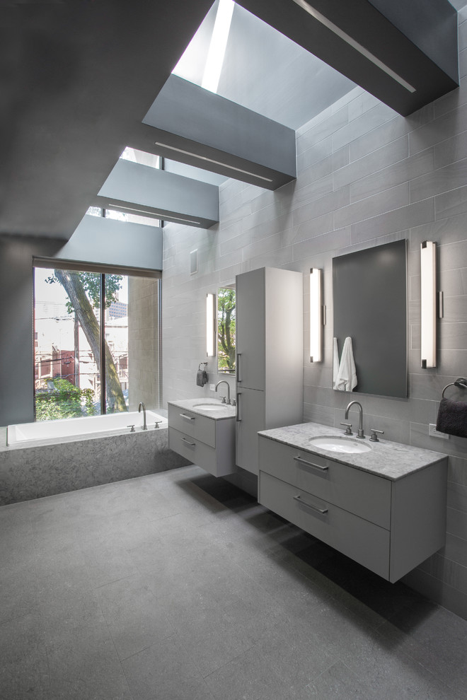 Ispirazione per una grande stanza da bagno padronale design con ante lisce, ante grigie, vasca sottopiano, piastrelle grigie, piastrelle in gres porcellanato, pareti grigie, pavimento con piastrelle in ceramica, lavabo sottopiano, top in quarzo composito, pavimento grigio e top grigio