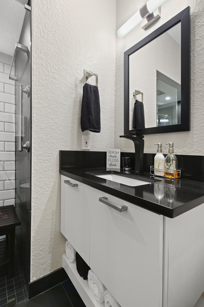 Example of a small minimalist master black and white tile and porcelain tile porcelain tile and black floor alcove shower design in Jacksonville with flat-panel cabinets, white cabinets, a wall-mount toilet, beige walls, an undermount sink, quartz countertops, a hinged shower door and black countertops