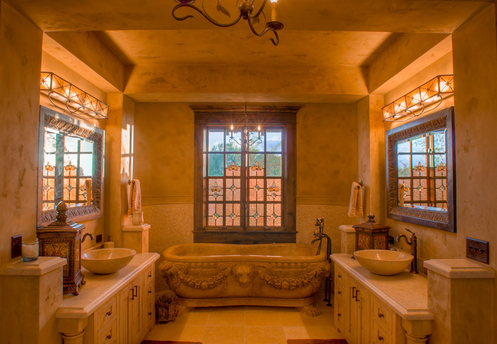 Diseño de cuarto de baño principal mediterráneo grande con armarios estilo shaker, puertas de armario de madera clara, encimera de piedra caliza, suelo de piedra caliza, lavabo sobreencimera, bañera exenta y baldosas y/o azulejos beige