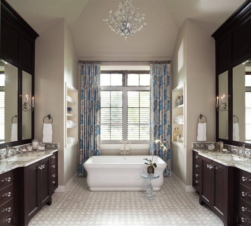 Стильный дизайн: главная ванная комната в классическом стиле с темными деревянными фасадами, столешницей из гранита, отдельно стоящей ванной, бежевыми стенами и врезной раковиной - последний тренд