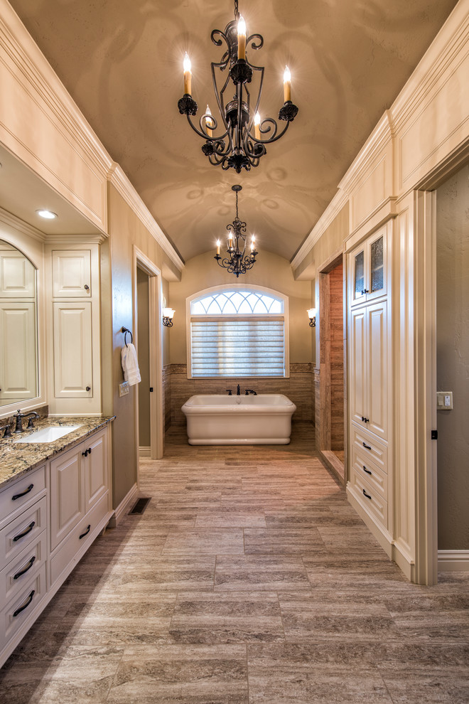 Inredning av ett klassiskt mycket stort en-suite badrum, med luckor med upphöjd panel, ett fristående badkar, ett undermonterad handfat, granitbänkskiva, vita skåp, en dusch i en alkov, brun kakel, porslinskakel, beige väggar och klinkergolv i porslin