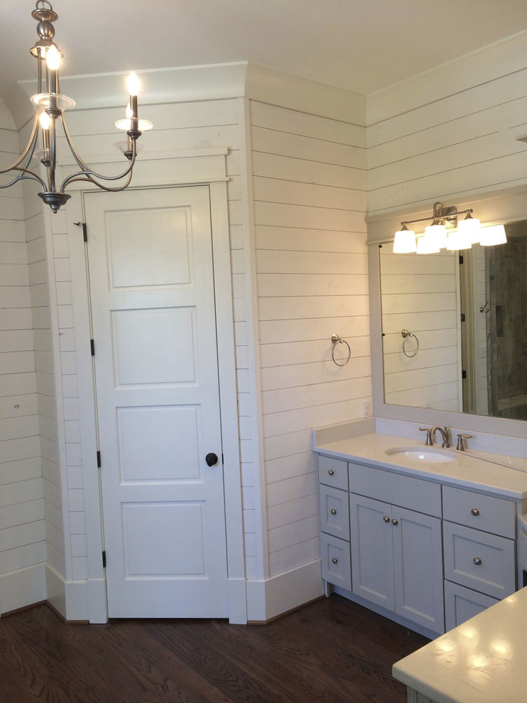 Modelo de cuarto de baño principal costero con lavabo bajoencimera, armarios con paneles empotrados, puertas de armario blancas, suelo de madera oscura y paredes blancas